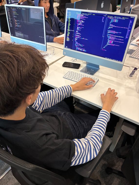 A student in a striped shirt writes code on an iMac